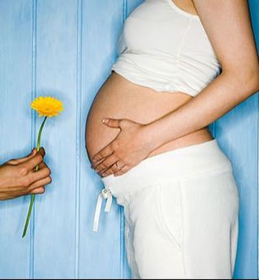 Picture of a lady holding her pregnant belly with a man on his knee giving her a flower